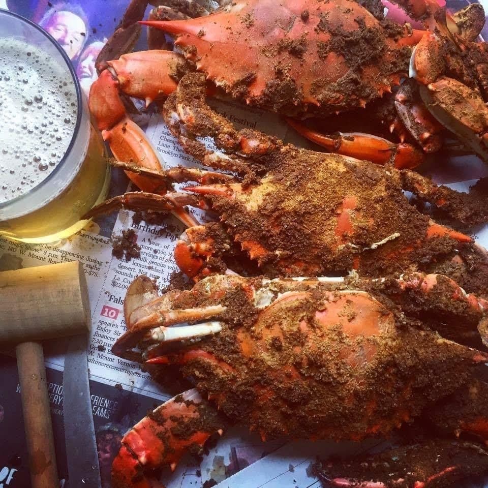 Crabs with seasoned shells on a newspaper-lined surface beside a glass of beer, ready to eat; messy spice coating visible on shells.